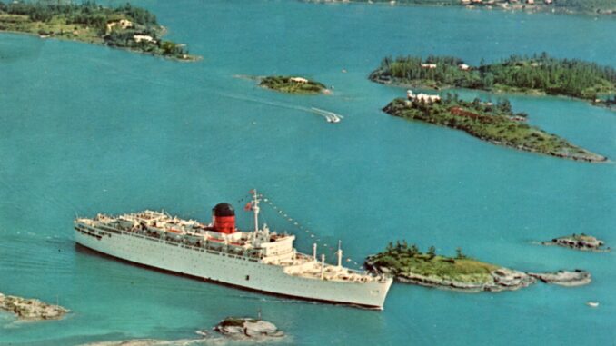 A white ship with a red and black funnel sails past small green islands.