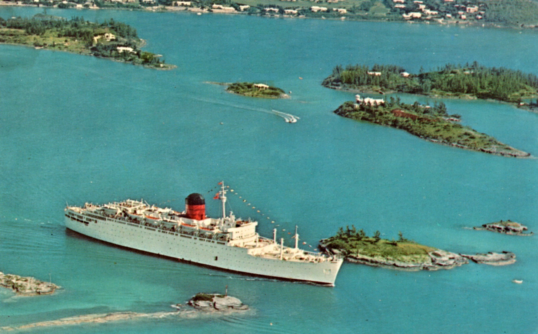 A white ship with a red and black funnel sails past small green islands.