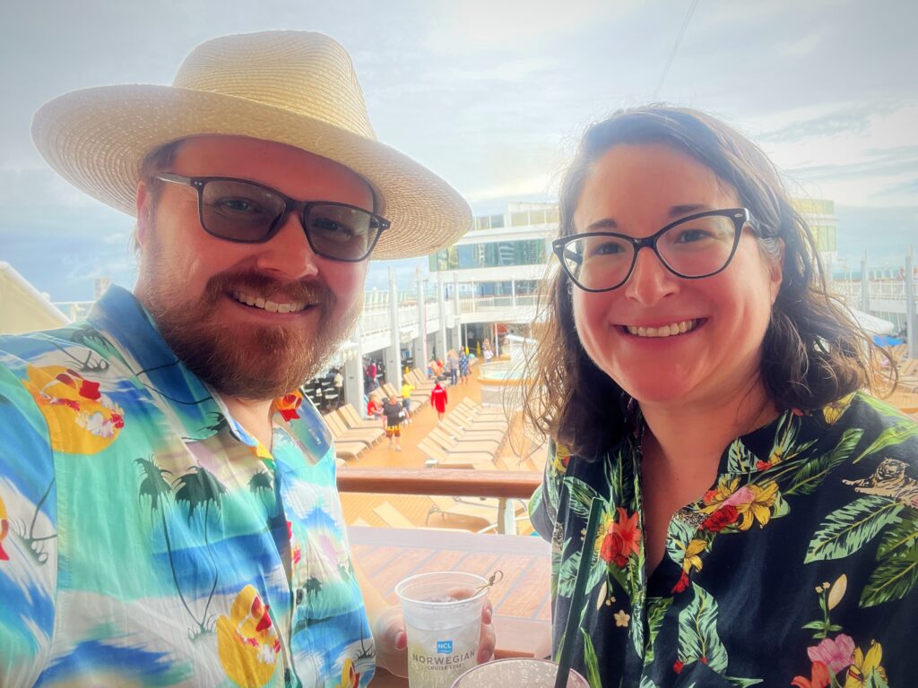A man and woman in tropical shirts smiling on a cruise ship.