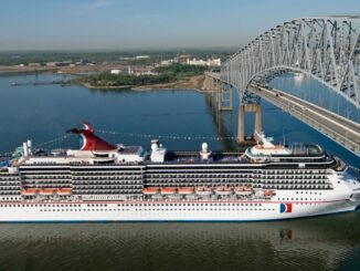 A white cruise ship with a red, white, and blue funnel sails under a steel frame bridge.