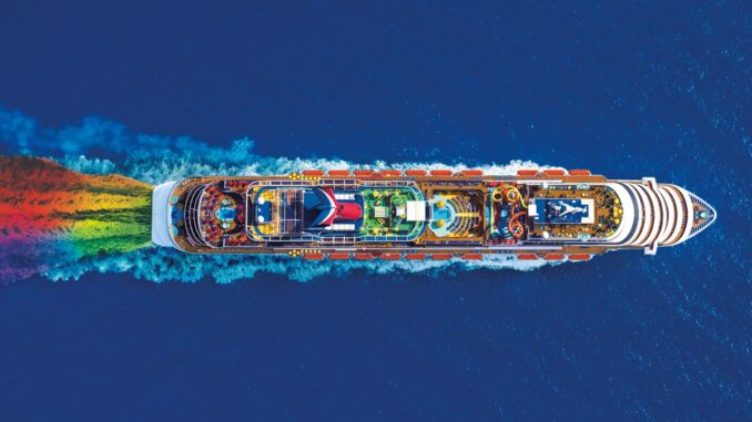 An aerial view of a cruise ship sailing with a rainbow wake.