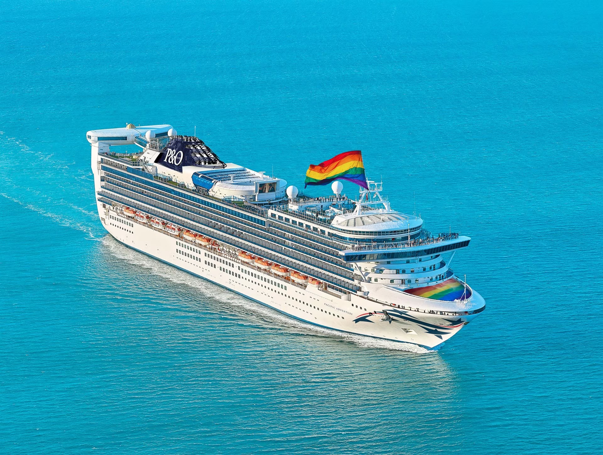 A white cruise ship flying a rainbow flag.