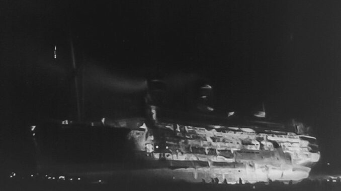 A burning shipwreck in the nighttime.