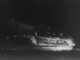A burning shipwreck in the nighttime.