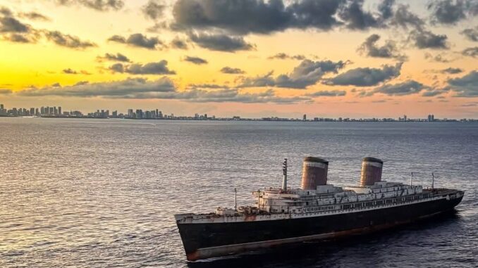 An ocean liner with two funnels being towed.