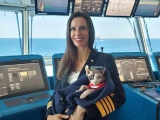 A woman in a ship's captain uniform holding a small hairless cat wrapped up in a blue blanket.