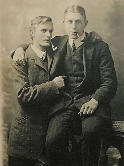 An old photo of two men with pipes cuddling each other.