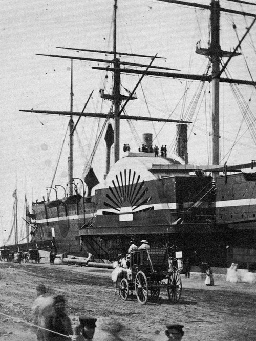 A giant paddle wheel ship docked at a pier as people mill about.