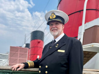 A photo of a uniformed man with a white beard standing in front of three red funnels.