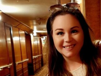 A smiling woman stands in front of a wood paneled hallway.