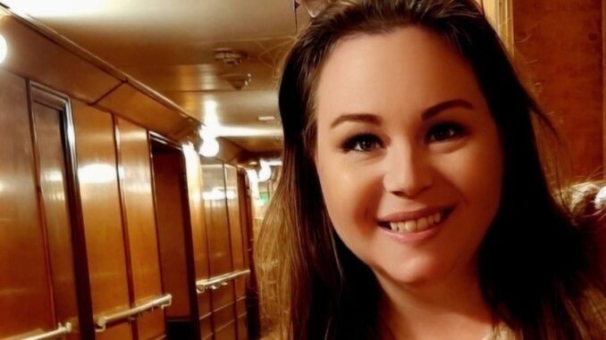 A smiling woman stands in front of a wood paneled hallway.