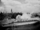 A black and white image of a giant ocean liner steaming into New York City.