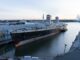 A rusty, decrepit ocean liner sits at a pier in the morning light.