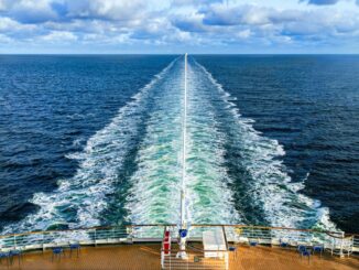 A ship at sea, with a long wake behind it.