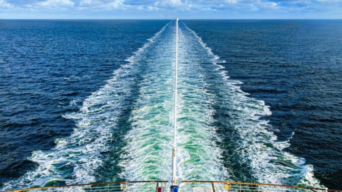 A ship at sea, with a long wake behind it.