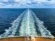 A ship at sea, with a long wake behind it.