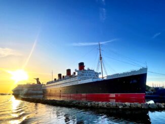 A black and red ocean liner at dock with the sun rising behind it.
