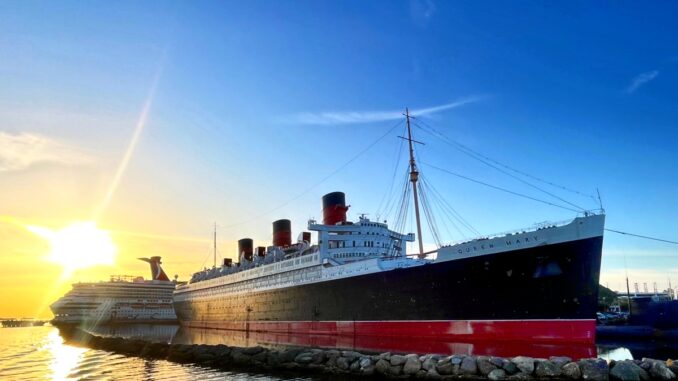 A black and red ocean liner at dock with the sun rising behind it.